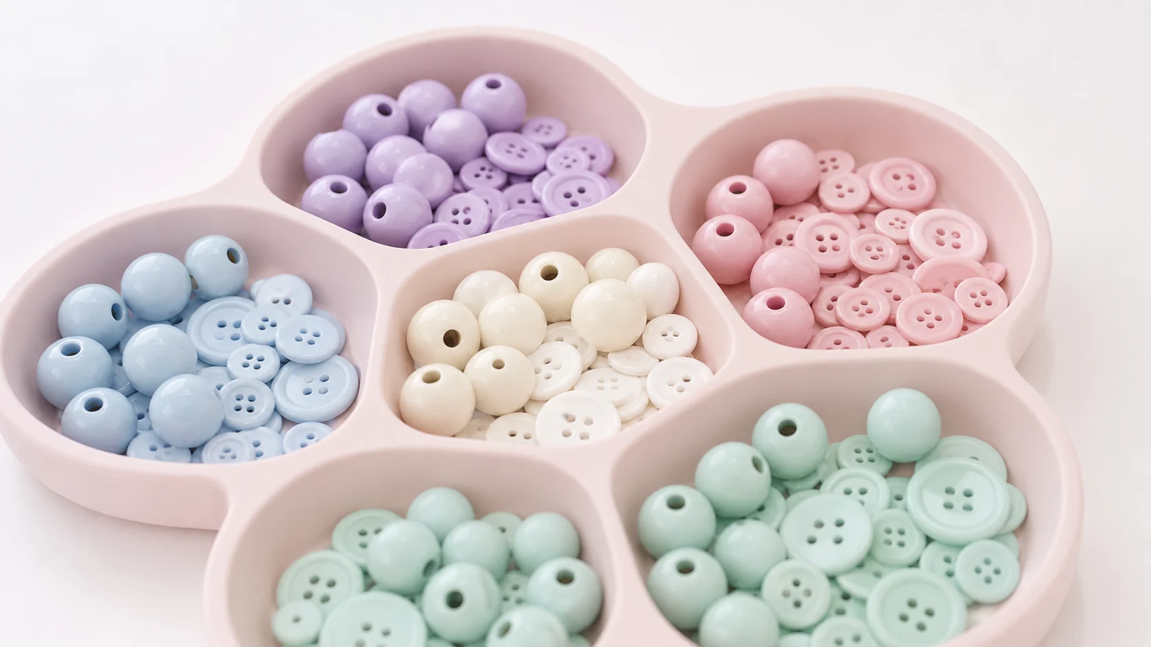 Pastel buttons and large smooth beads sorted by color in a blush-pink tray.